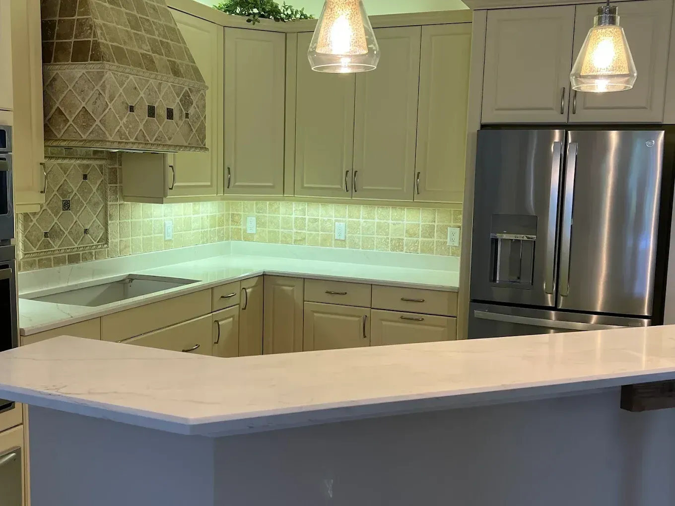 Modern kitchen with cream cabinets, white countertops, pendant lights, and stainless steel refrigerator