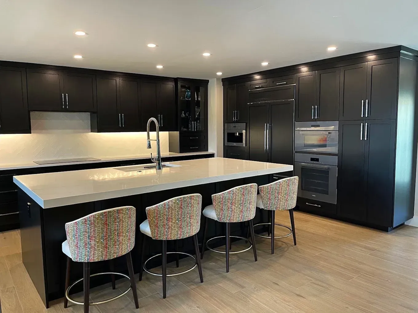Modern black-and-white kitchen with large island, bar stools, built-in oven, and stainless steel appliances
