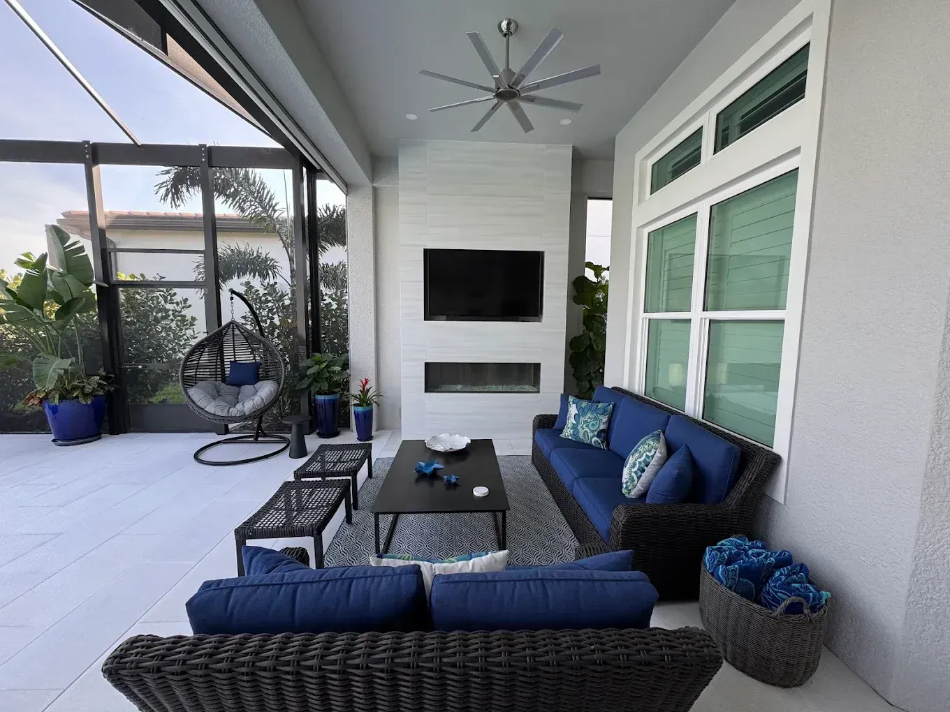 Modern covered patio with blue seating, coffee table, ceiling fan, and large sliding windows.