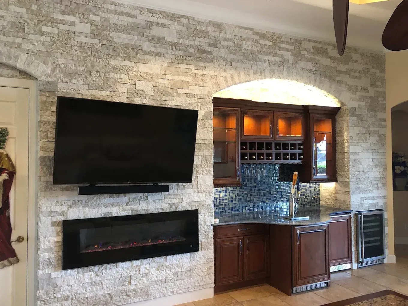 Modern living room with stone fireplace, wall-mounted TV, and built-in wet bar with wood cabinets
