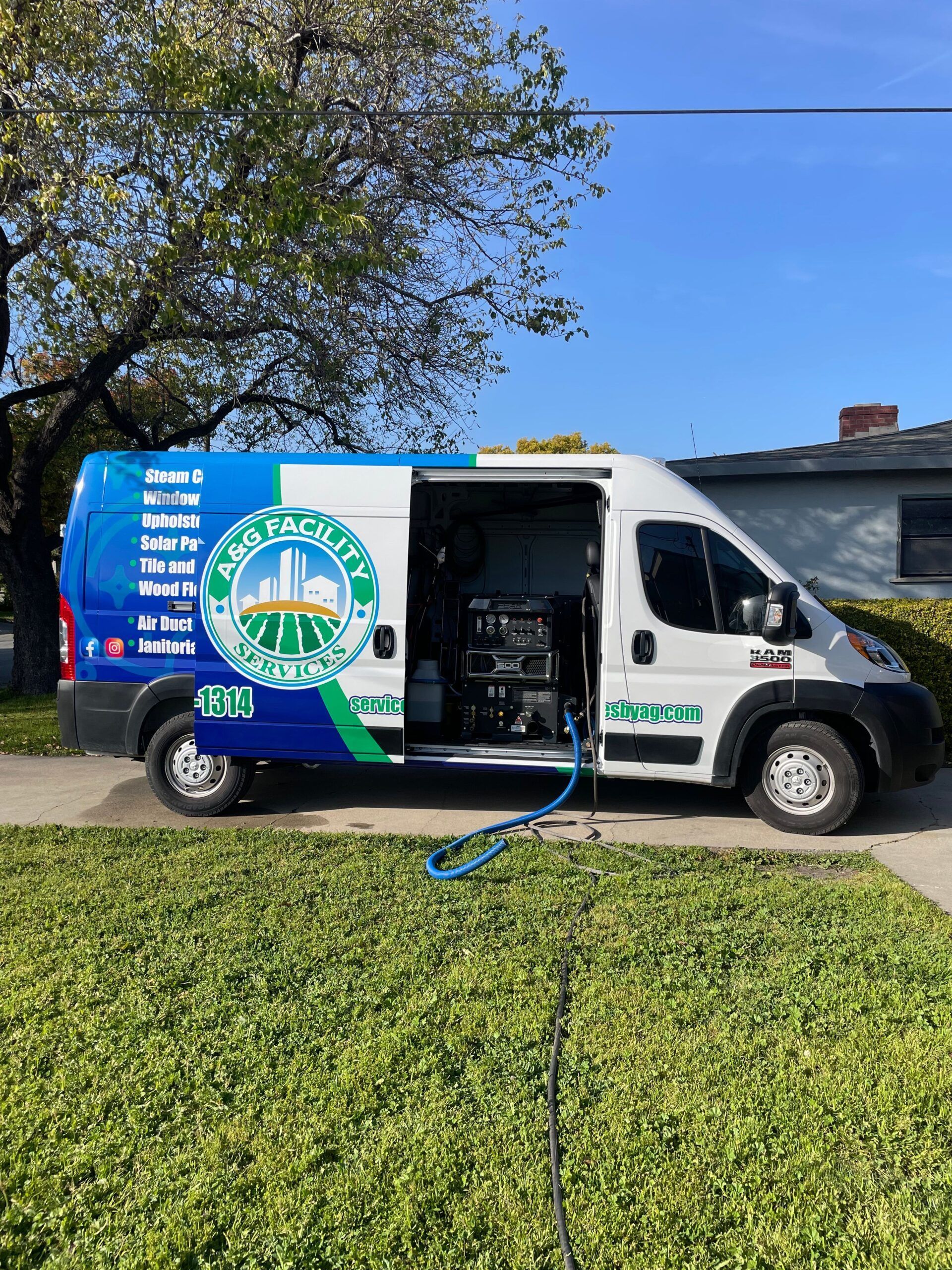 A white and blue van with company logo parked on a street, hose extending to a lawn.