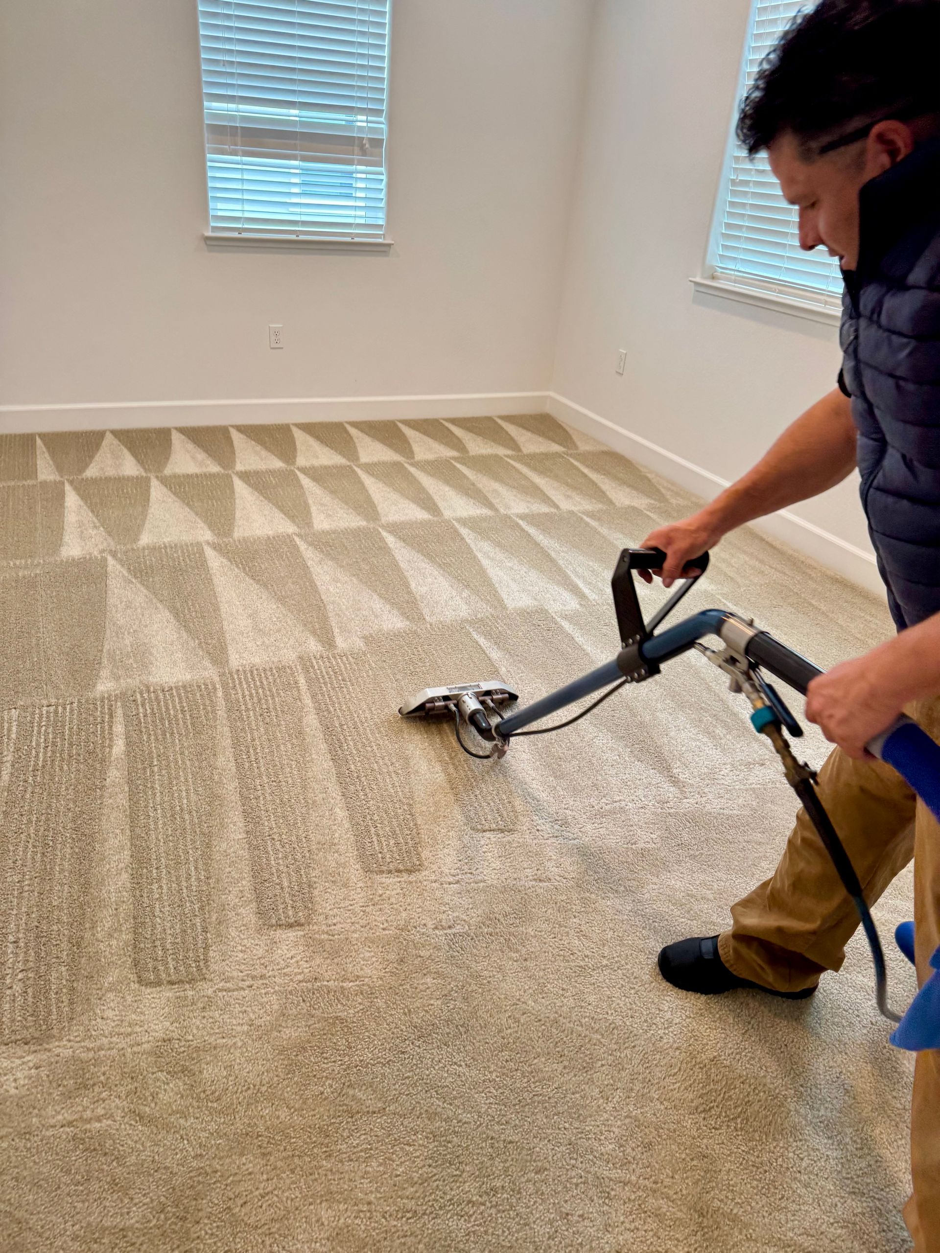 Person cleaning beige carpet with a professional machine in a room with a window.