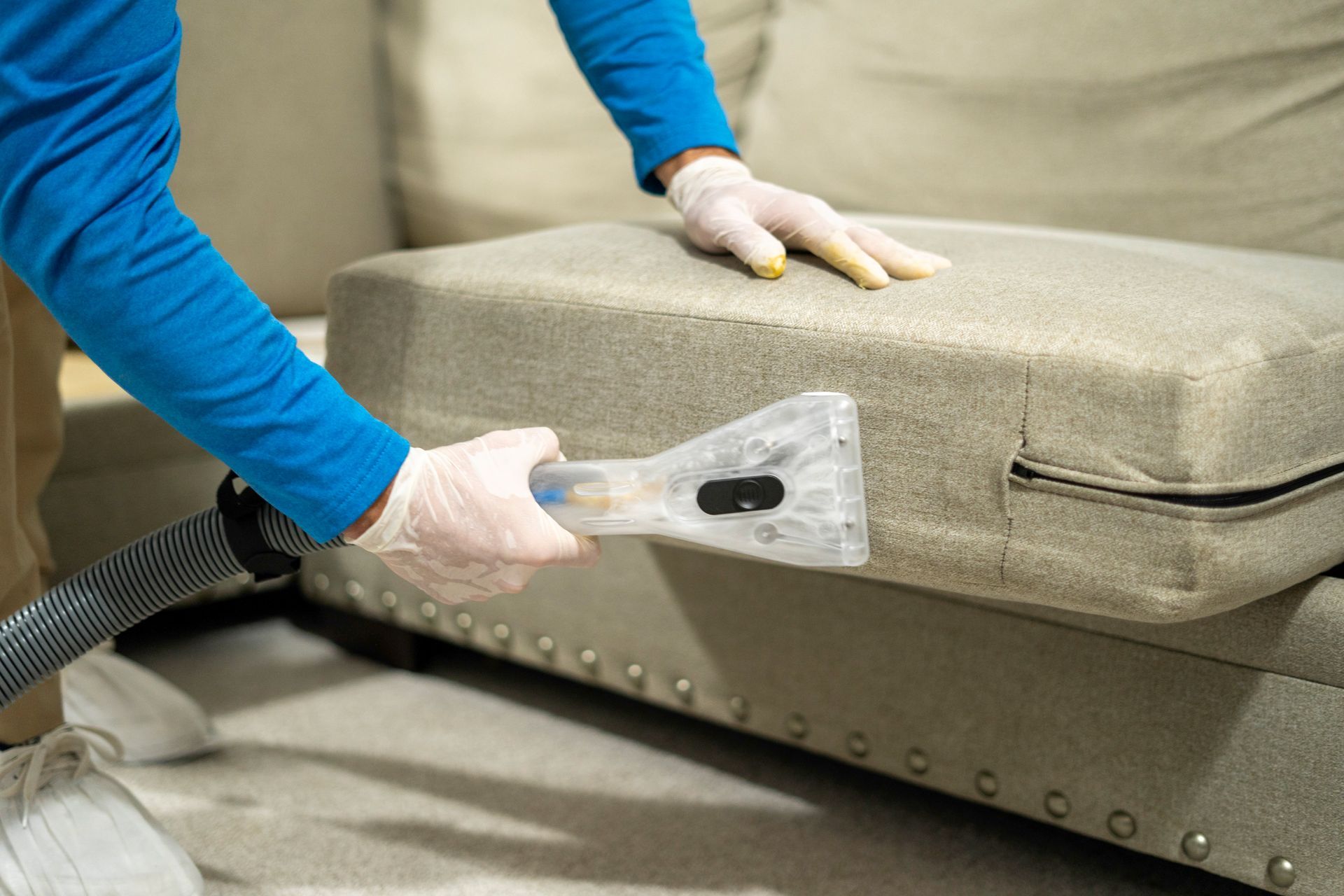 A person is cleaning a couch with a vacuum cleaner.