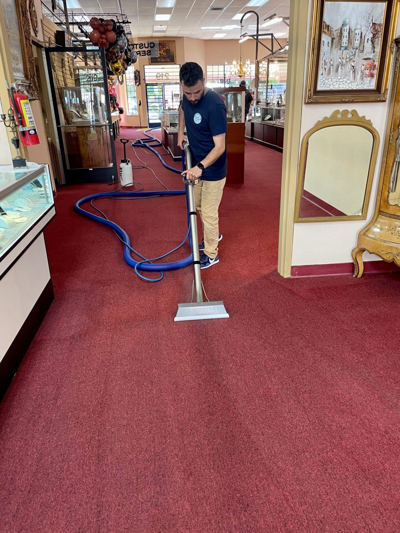 A man is using a vacuum cleaner to clean a red carpet in a store.