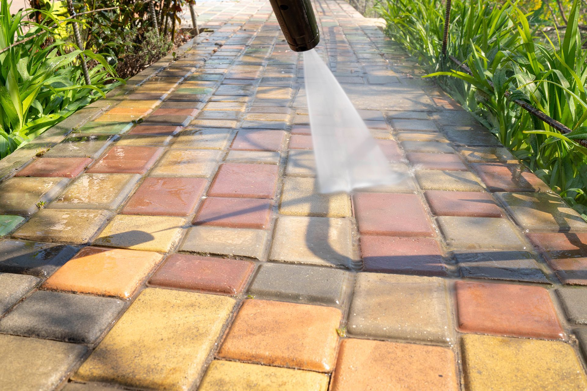 A person is cleaning a brick walkway with a high pressure washer.