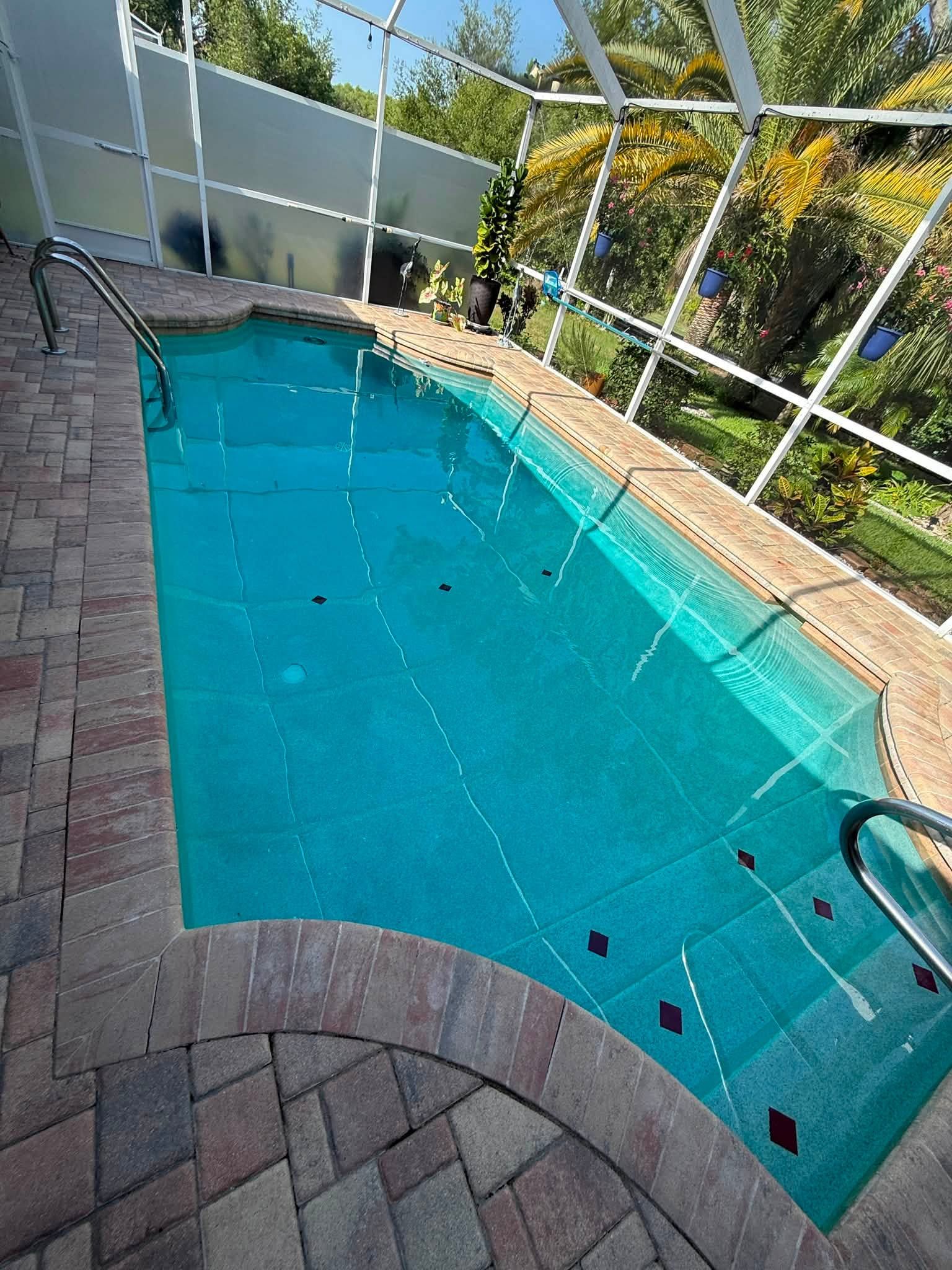 Screened backyard swimming pool with blue water, brick patio, and trees beyond the enclosure