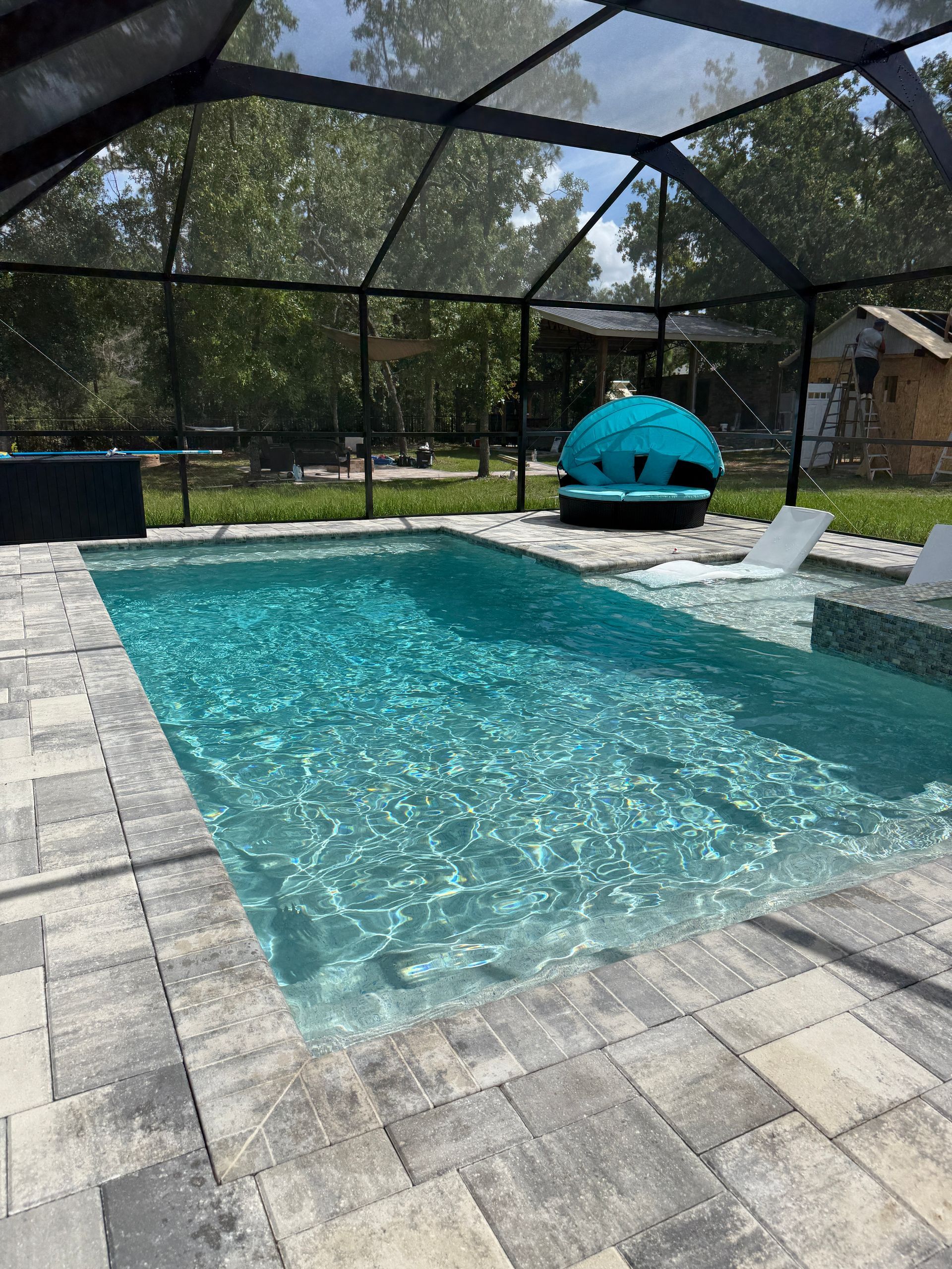 Pool with clear turquoise water, surrounded by gray paving stones, under a screened enclosure.