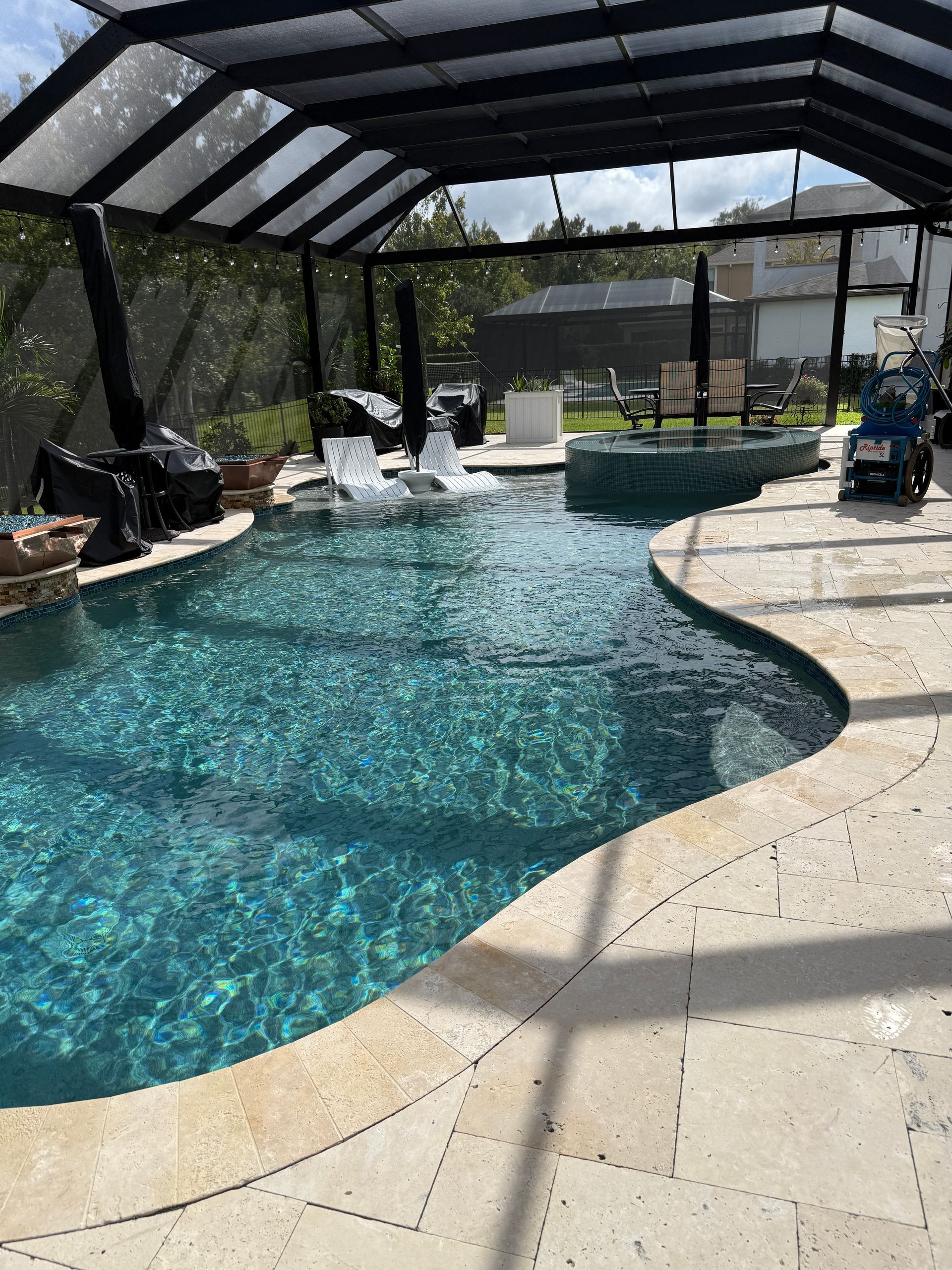 Pool with waterfall feature and a screen enclosure, surrounded by beige stone pavers.