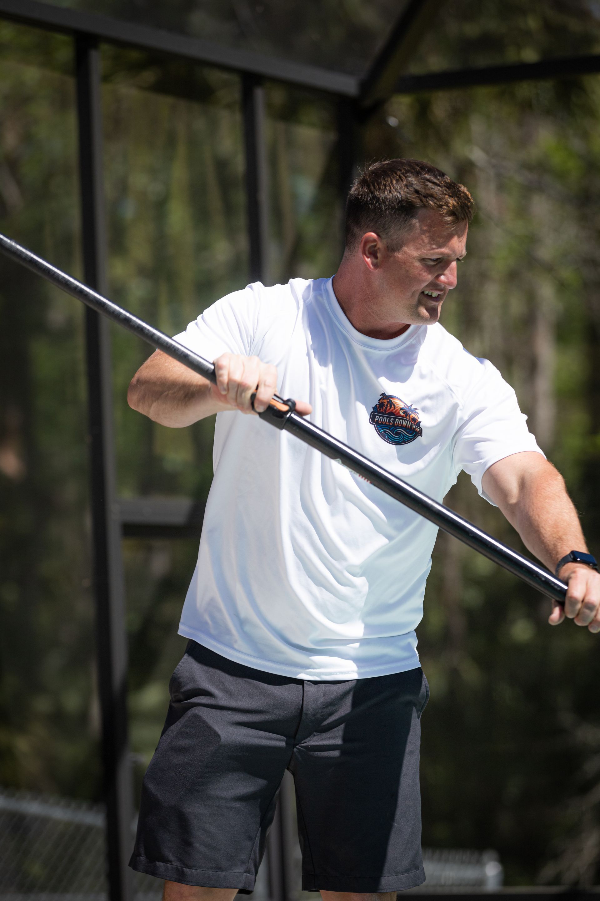 Man in white shirt and black shorts holding a long, dark pole.