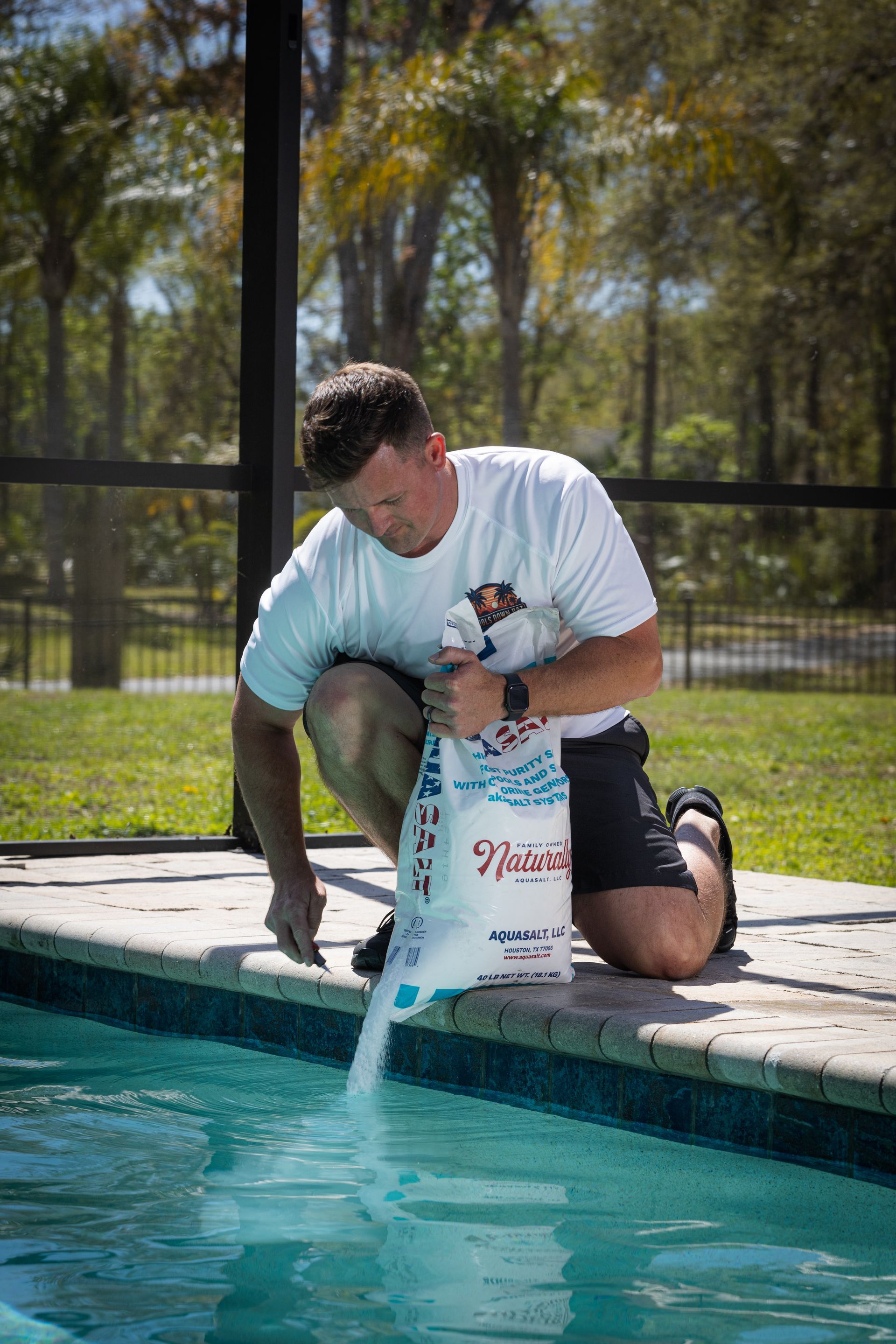 Man pouring pool chemical from a bag into a swimming pool. Outdoors, sunny.