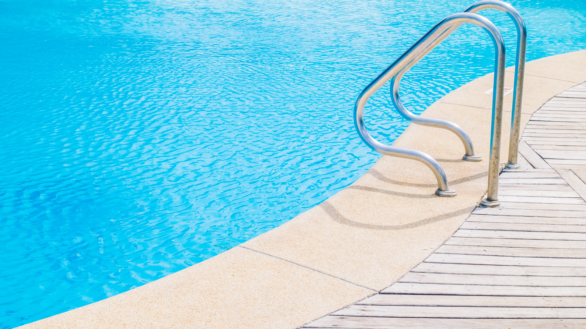 Swimming pool ladder beside clear blue water and a curved white pool edge