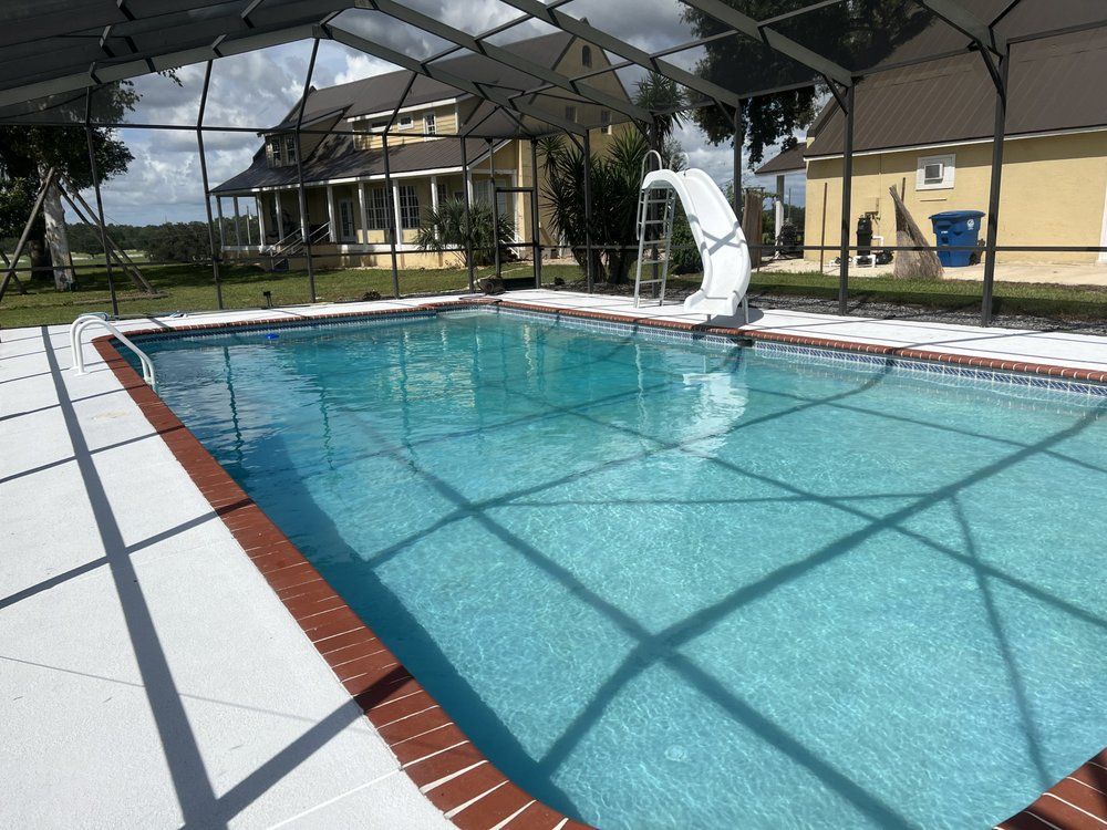 Outdoor swimming pool with clear blue water, white deck, and shade canopy beside houses.