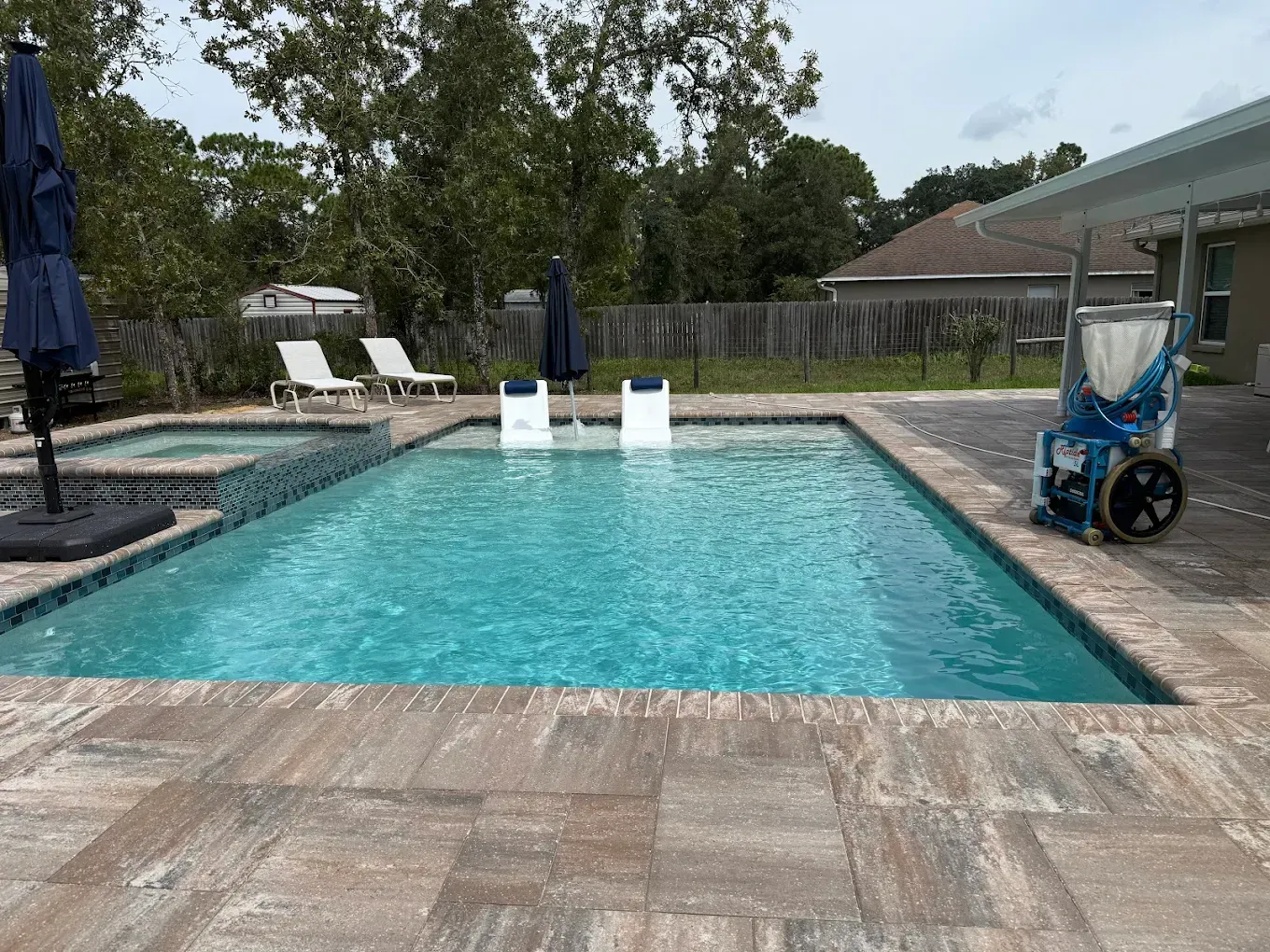 Backyard swimming pool with turquoise water, lounge chairs, umbrellas, and a stroller on the deck