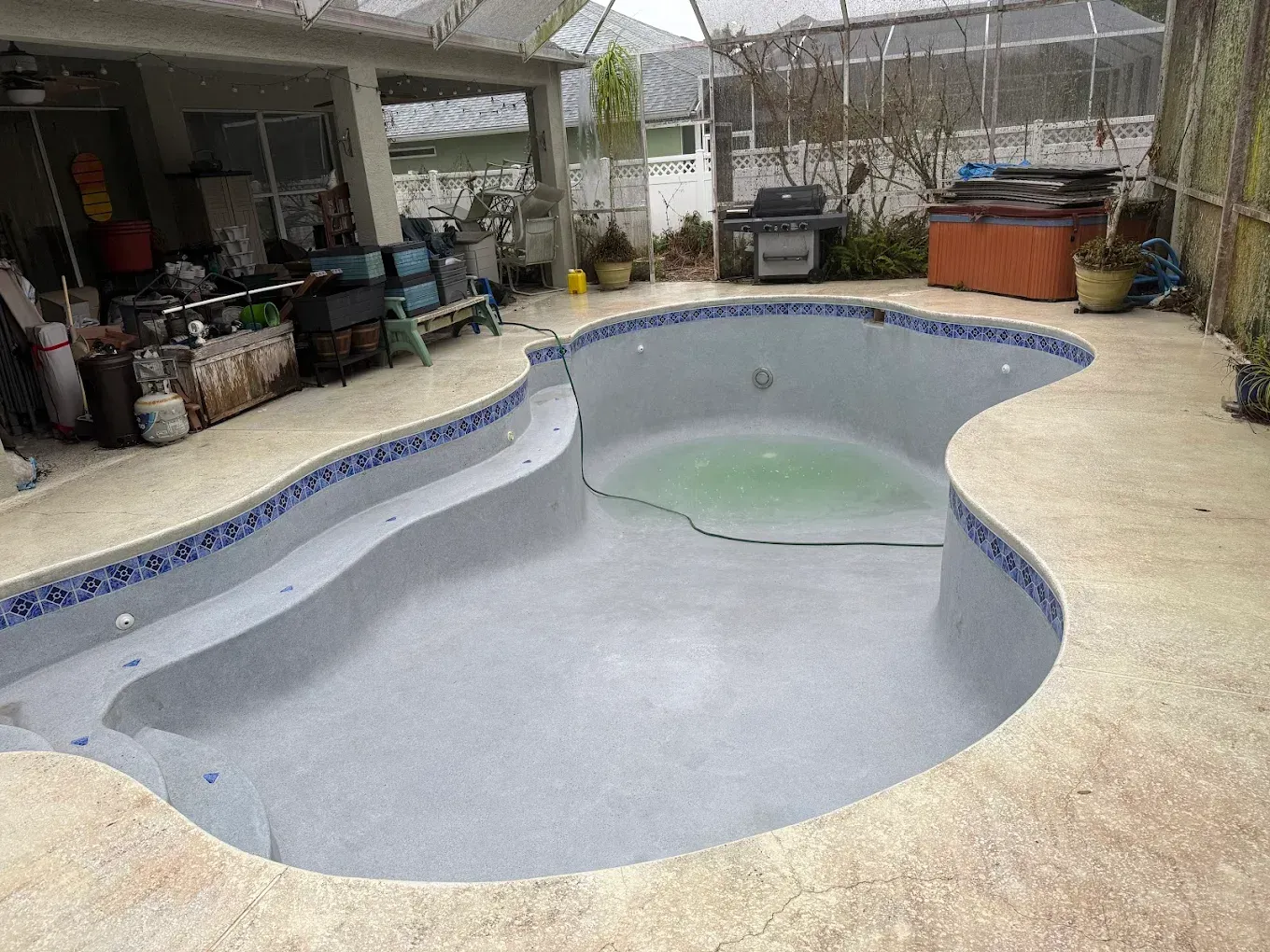 Empty backyard swimming pool with gray interior and beige deck, shaded patio in the background
