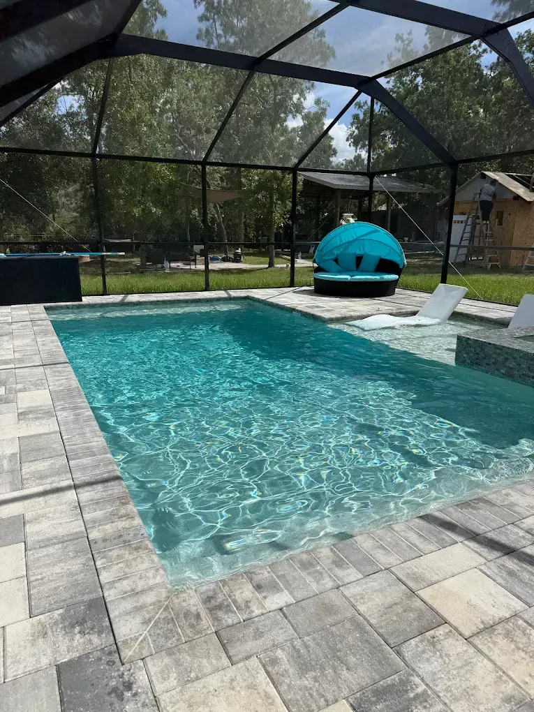 Screened backyard pool with turquoise water, paver deck, and a blue cushioned lounger under a black enclosure