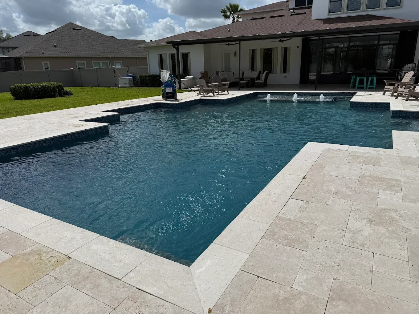 Backyard swimming pool beside a patio and house under a cloudy sky