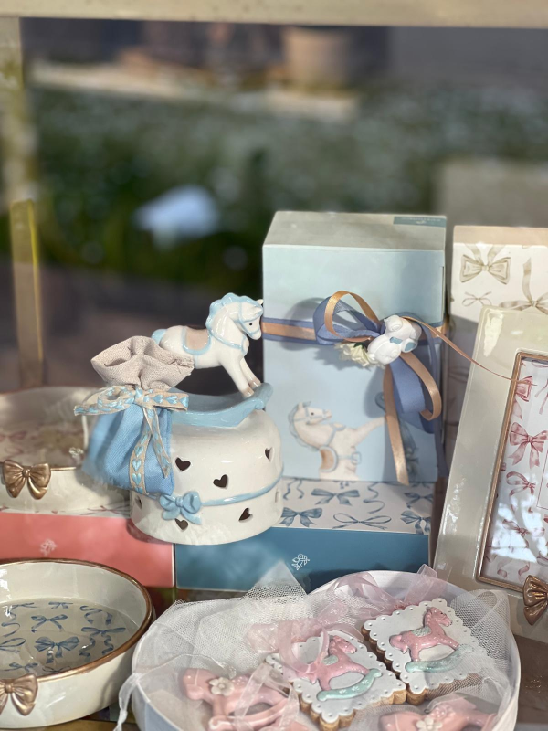 Espositore regalo dai colori pastello con scatola decorata con nastro, piccole statuette e dolcetti incartati su un tavolo.
