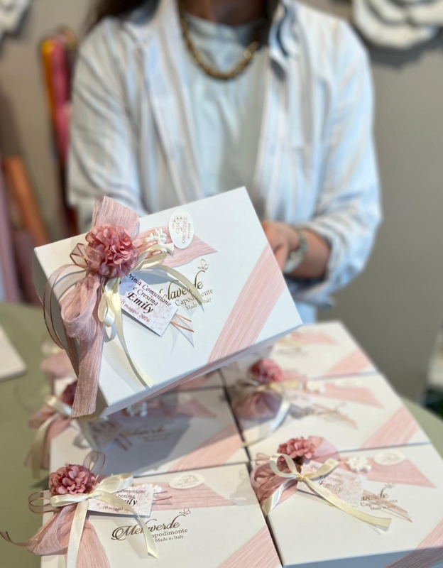 Persona che tiene in mano scatole per inviti di nozze rosa pastello decorate con nastri e fiori