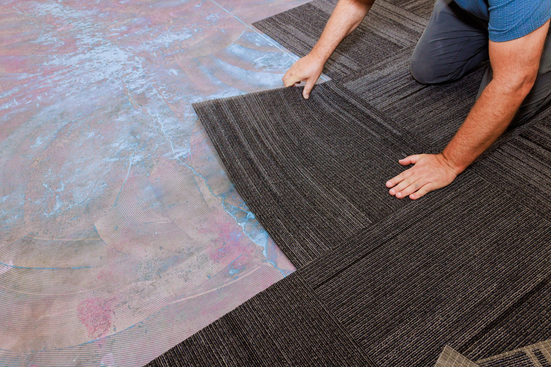 Person laying dark floor mats over a marbled floor surface