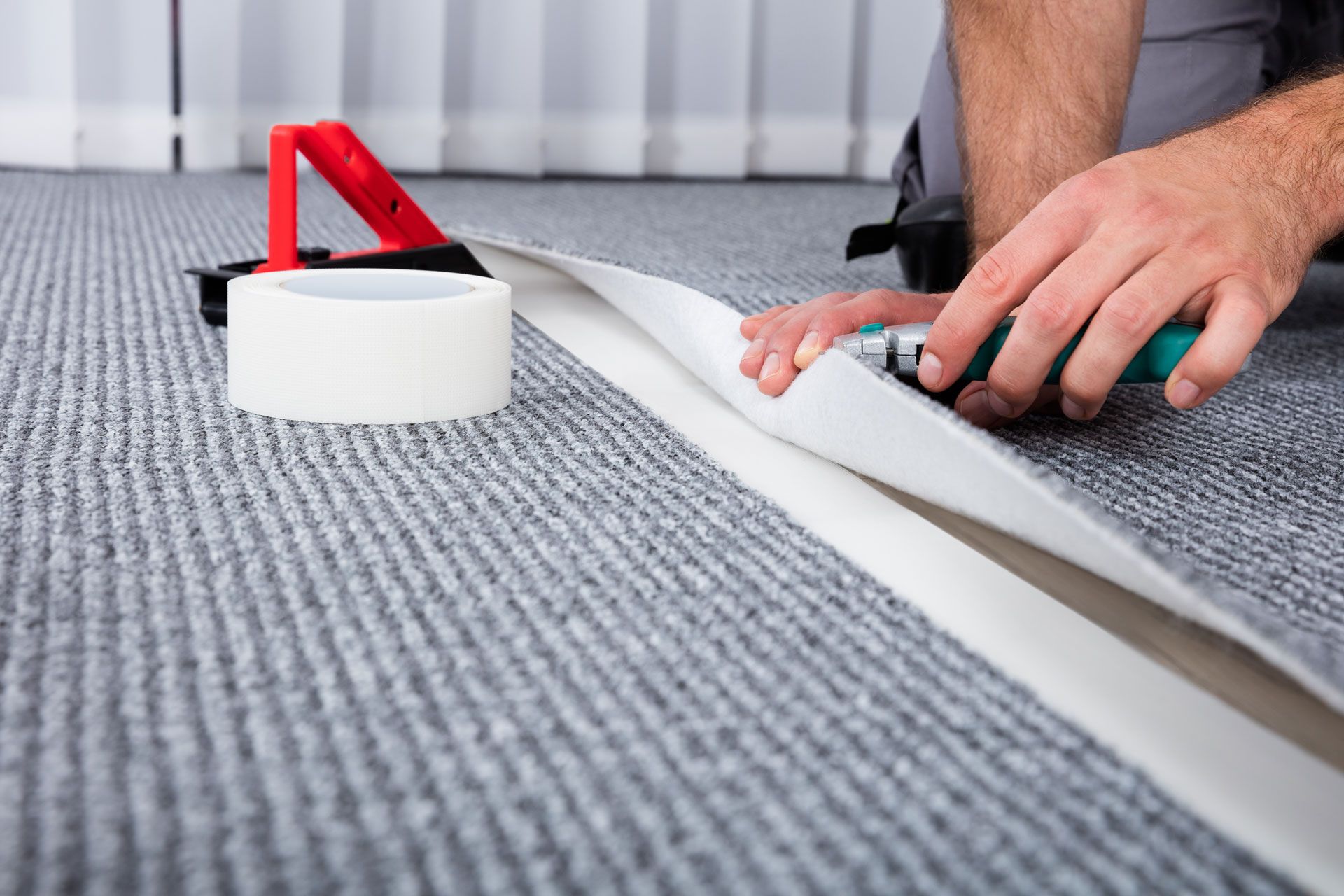 Hands applying tape to a carpet seam with a red tape dispenser