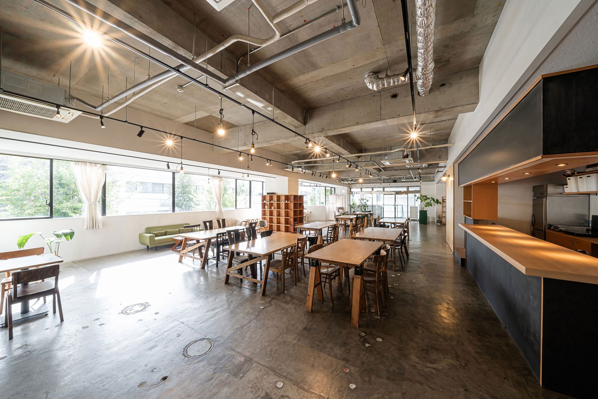 Modern office lounge with wooden tables, chairs, large windows, and an exposed ceiling