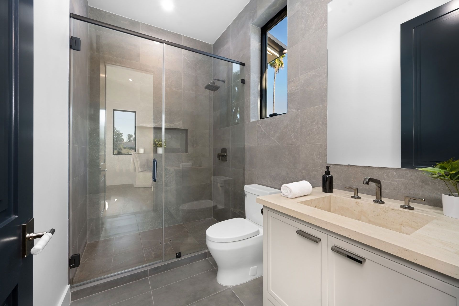 Modern bathroom with glass shower, toilet, and vanity with beige countertop and dark fixtures