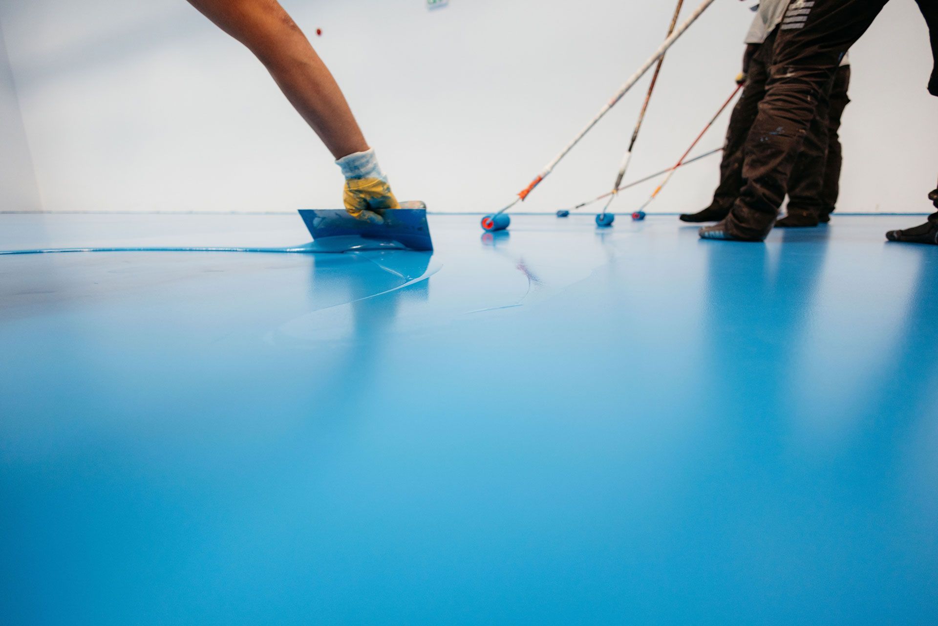 Two people painting a bright blue floor with rollers and masking tape edges