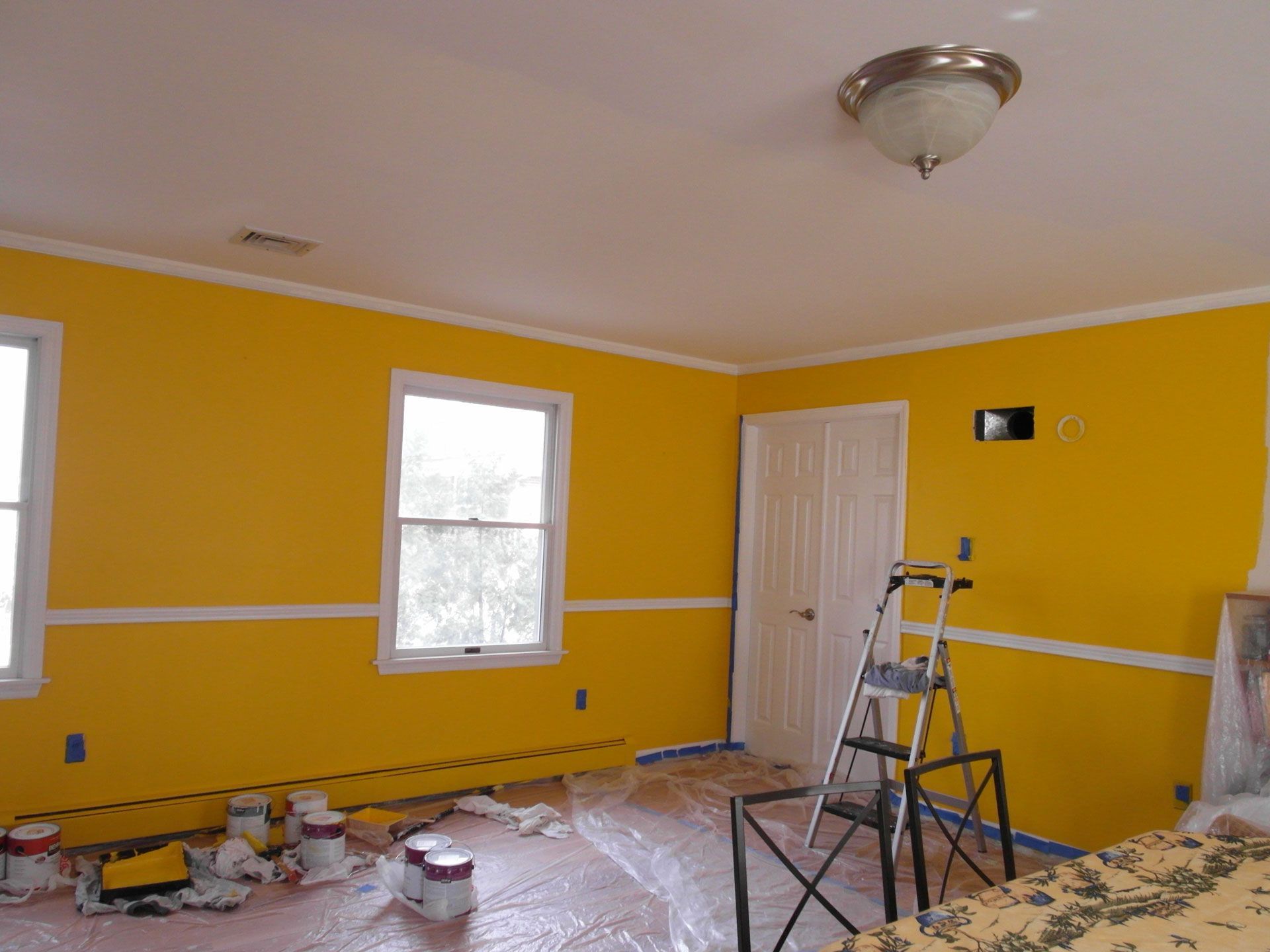 Yellow room under renovation with paint supplies, step ladder, and covered floor