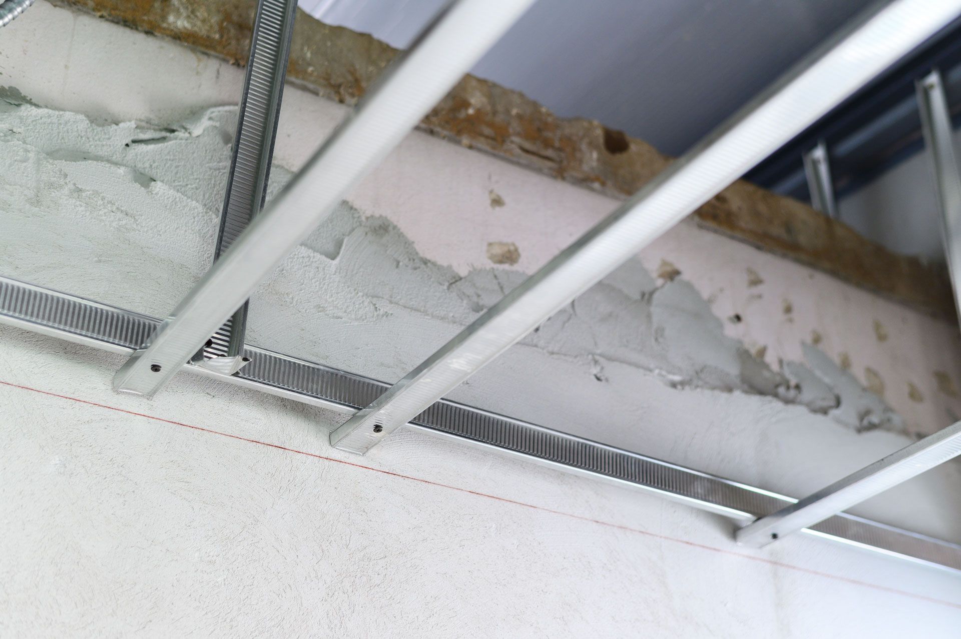 Damaged white ceiling with peeling paint and exposed metal framing near a staircase