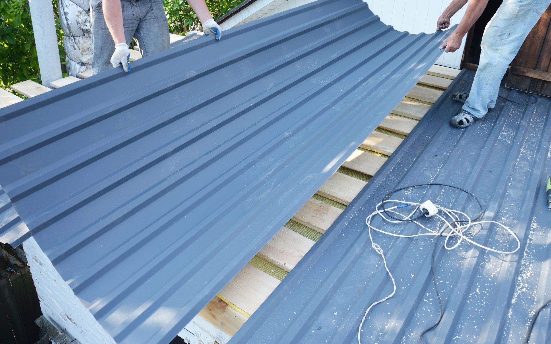 Workers installing blue corrugated metal roofing panels on a house roof