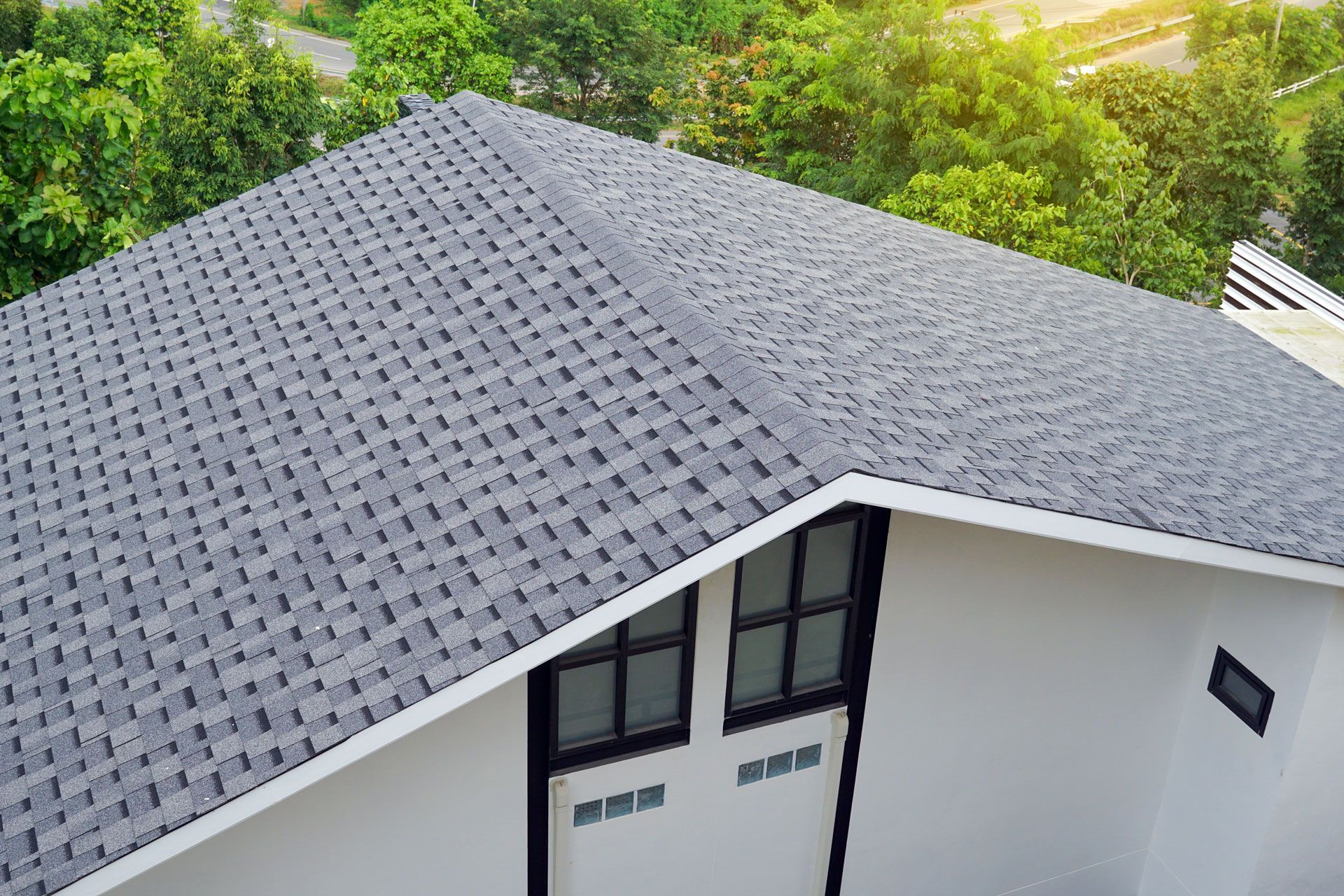 Gray shingled roof on a white house, viewed from above with green trees in the background