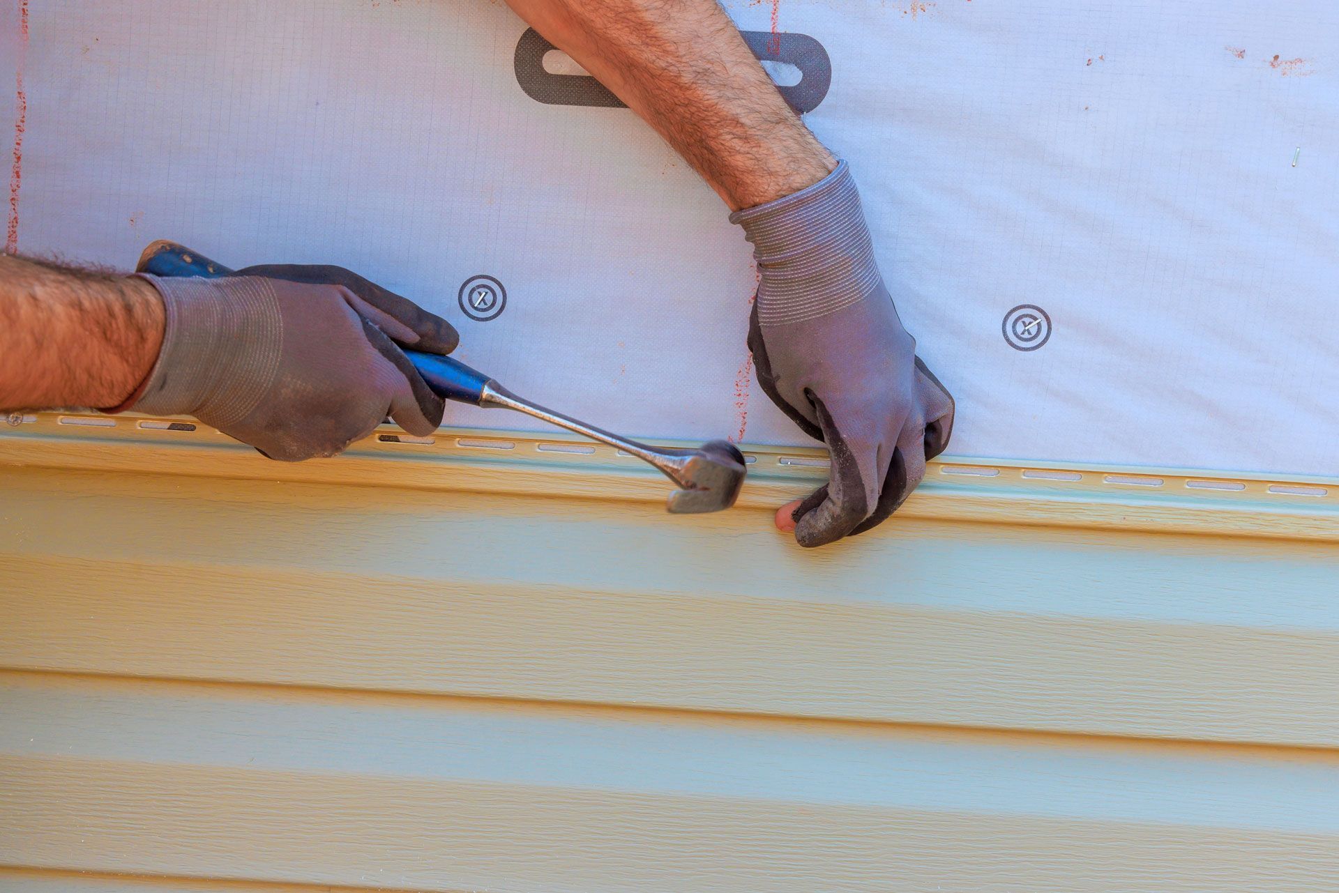 Gloved hands using a tool to seal a seam on a white wall or panel at a construction site