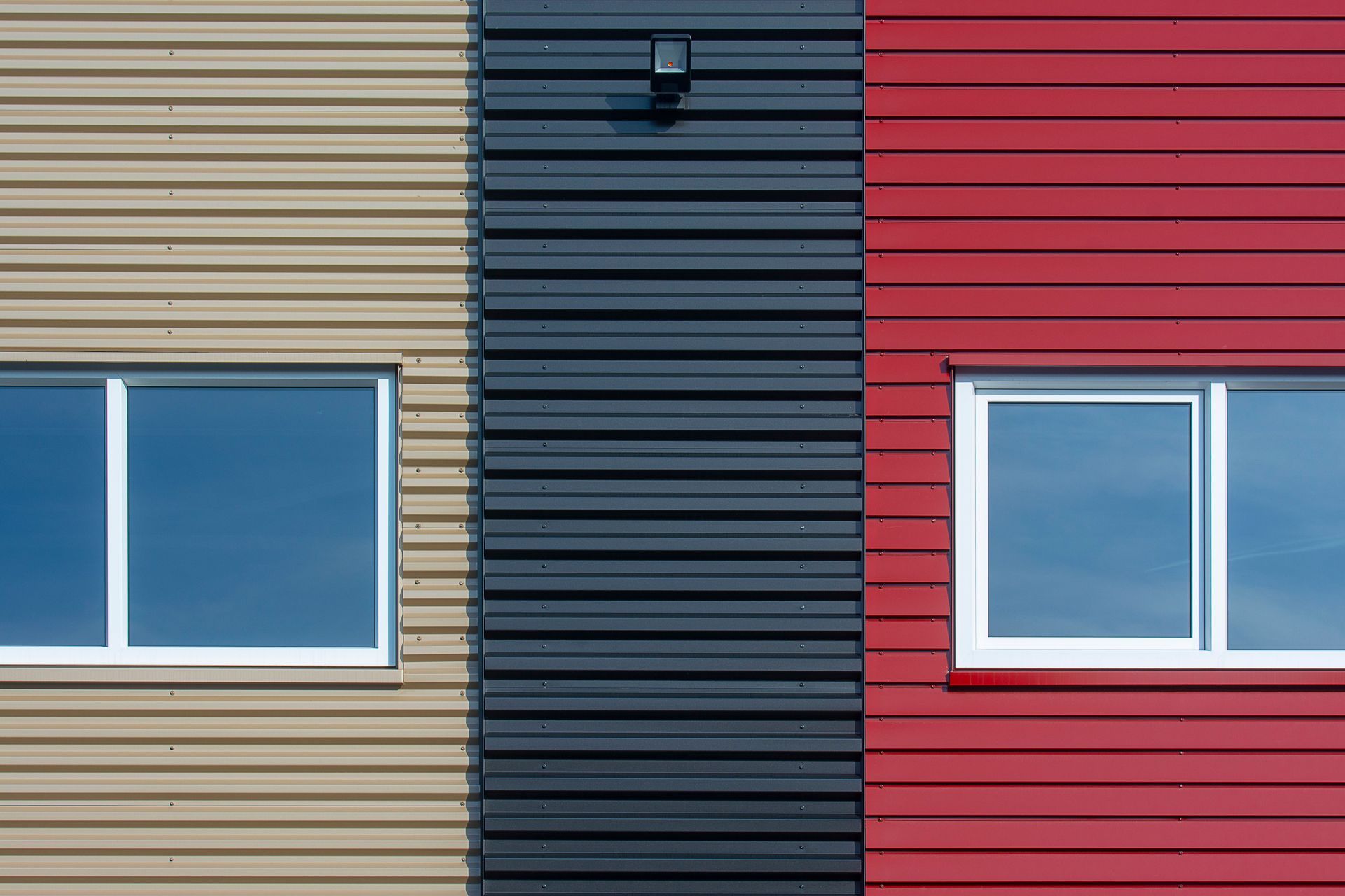 Colorful building facade with beige, dark blue, and red siding and two windows