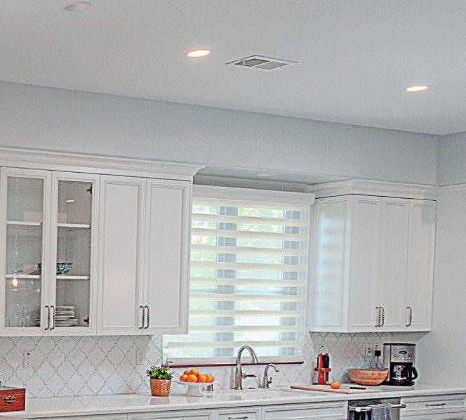 Bright modern kitchen with white cabinets, window blinds, and a sink beneath the window