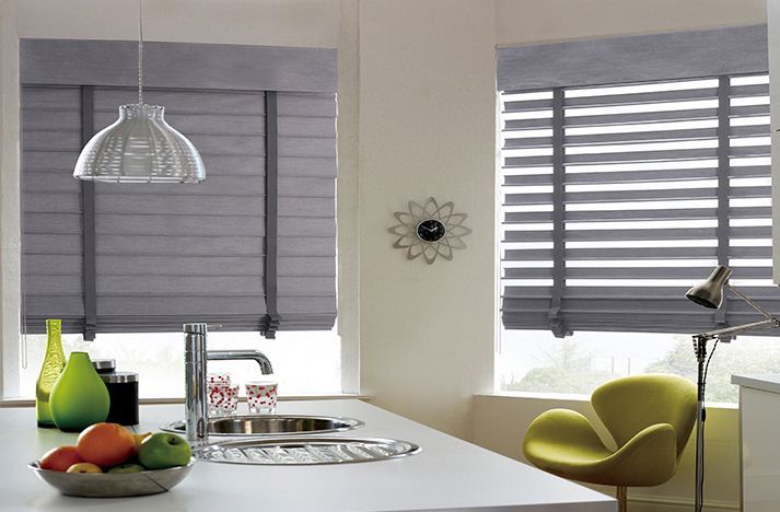Modern kitchen with gray blinds, white island, fruit bowl, pendant light, and green chair by the window