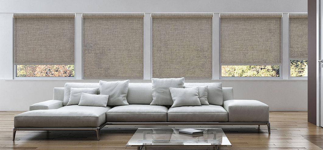 Modern living room with a gray sectional sofa, glass coffee table, and large window blinds.