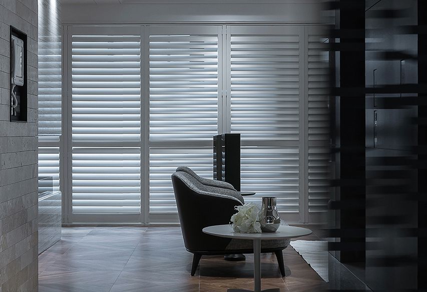 Modern living room with black chair, small table, and white blinds across large windows