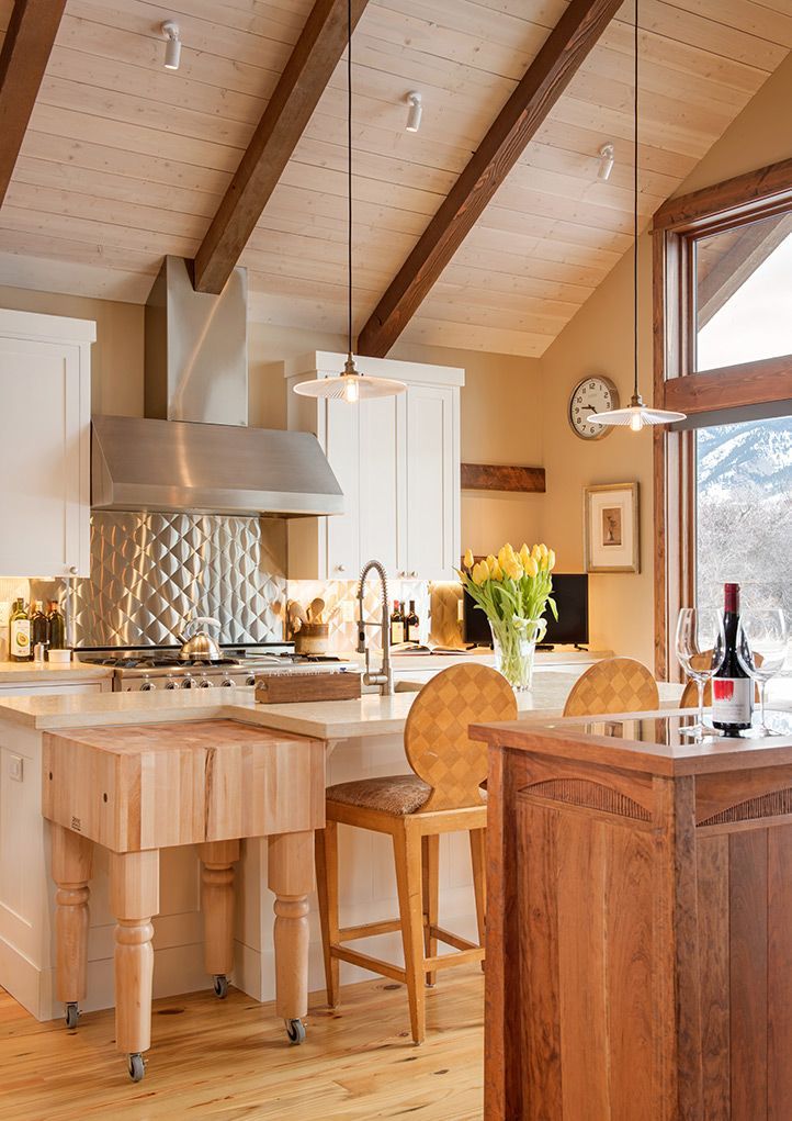 Bright rustic kitchen with wood cabinets, island, stools, and mountain view windows