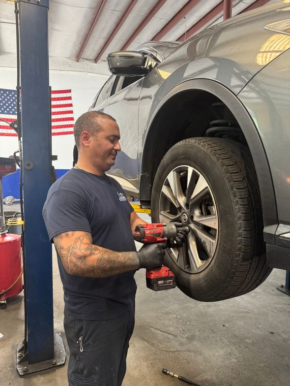 Mechanic tightening lug nuts on a raised gray SUV in a shop