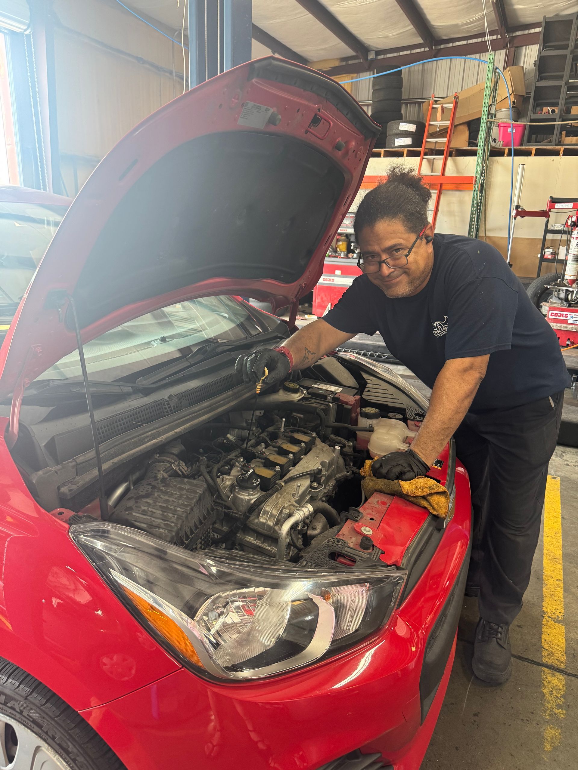 Person inspecting a red car’s engine with the hood open in a garage