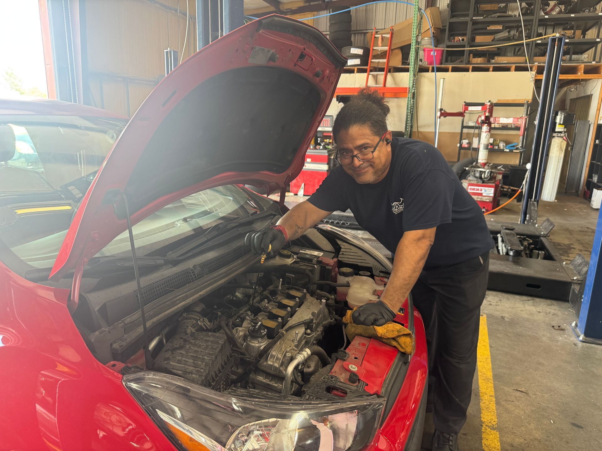 Mechanic working on a red car with the hood open in an auto repair shop