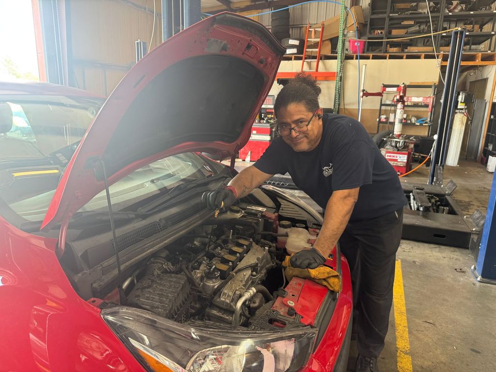 Mechanic working on a red car with the hood open in an auto repair shop