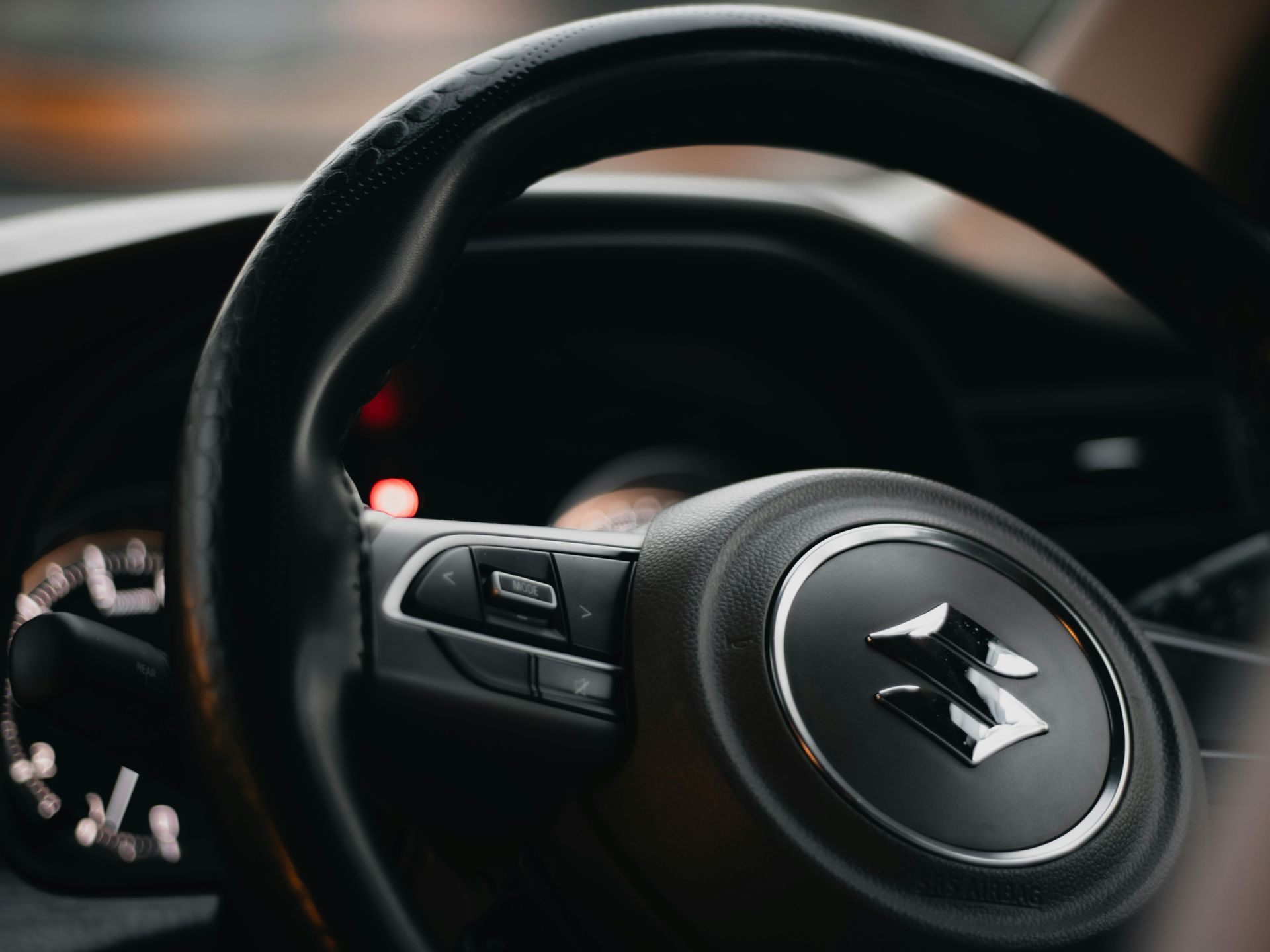 Close-up of a black car steering wheel with the Suzuki logo and dashboard controls