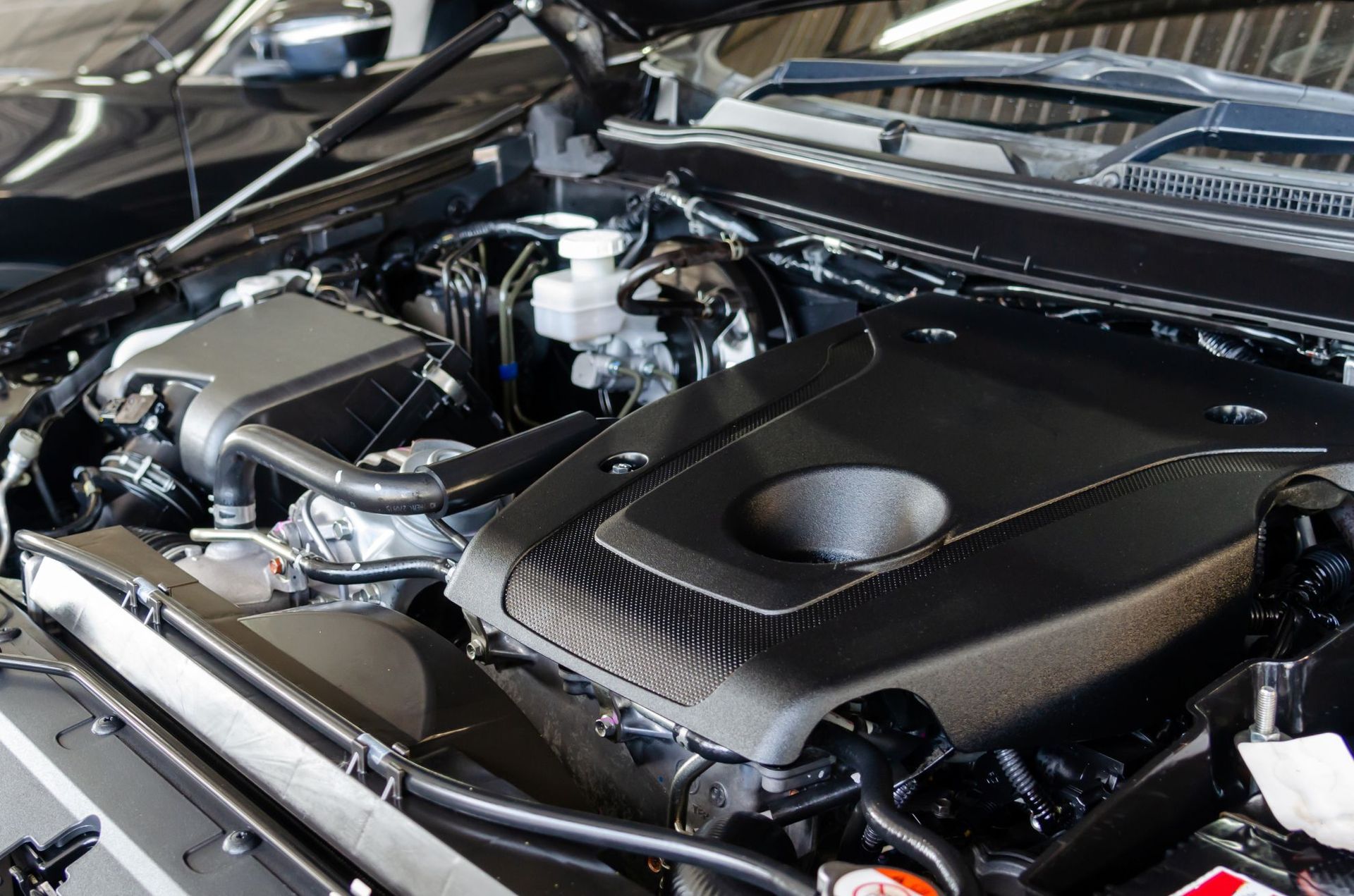 Close-up of a car engine bay with a black cover and silver components under the hood