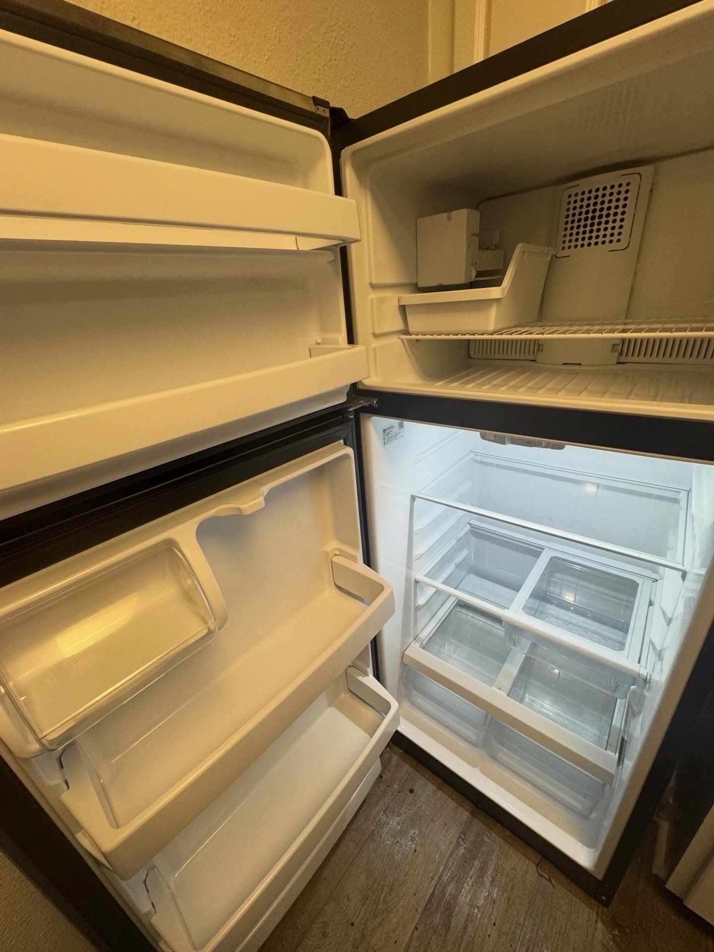 An empty, clean, white two-door refrigerator with freezer compartment on top and open doors.