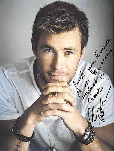 Chris Hemsworth with hands clasped, wearing bracelets and watch, smiling, signed autograph, white shirt.