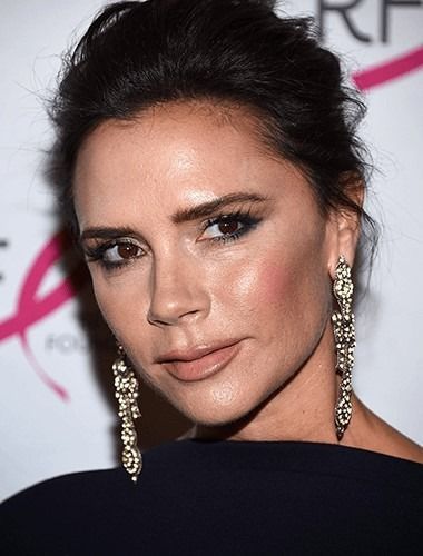 Woman with dark hair in updo, wearing large jeweled earrings, and makeup; looking toward the camera.