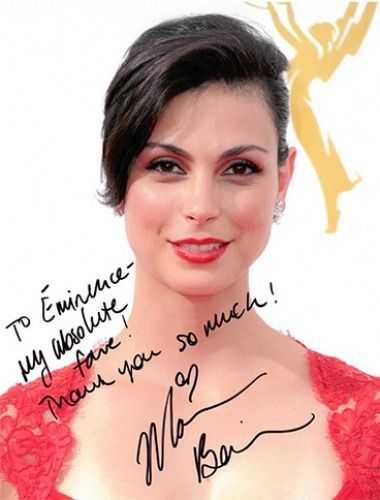 Woman with dark hair, red lips, and a red dress, smiling, holding an autograph.