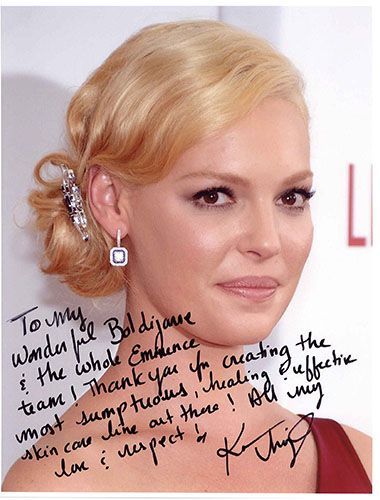 Katherine Heigl with blonde hair, signed photo, promoting skincare line, smiling.