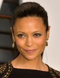 Woman with dark hair pulled back, wearing earrings and a black top with gold embellishments; looking forward.